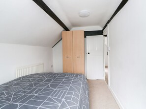 A bedroom with a bed, a radiator, a wooden wardrobe, and a white door. - Oar Cottage (Mablethorpe)