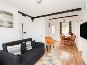Una habitación con un sofá negro, una mesa de comedor con sillas, un televisor y una puerta que da a un balcón.