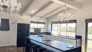 Een moderne keuken met een groot eiland, barstoelen, een kroonluchter en uitzicht door de ramen.