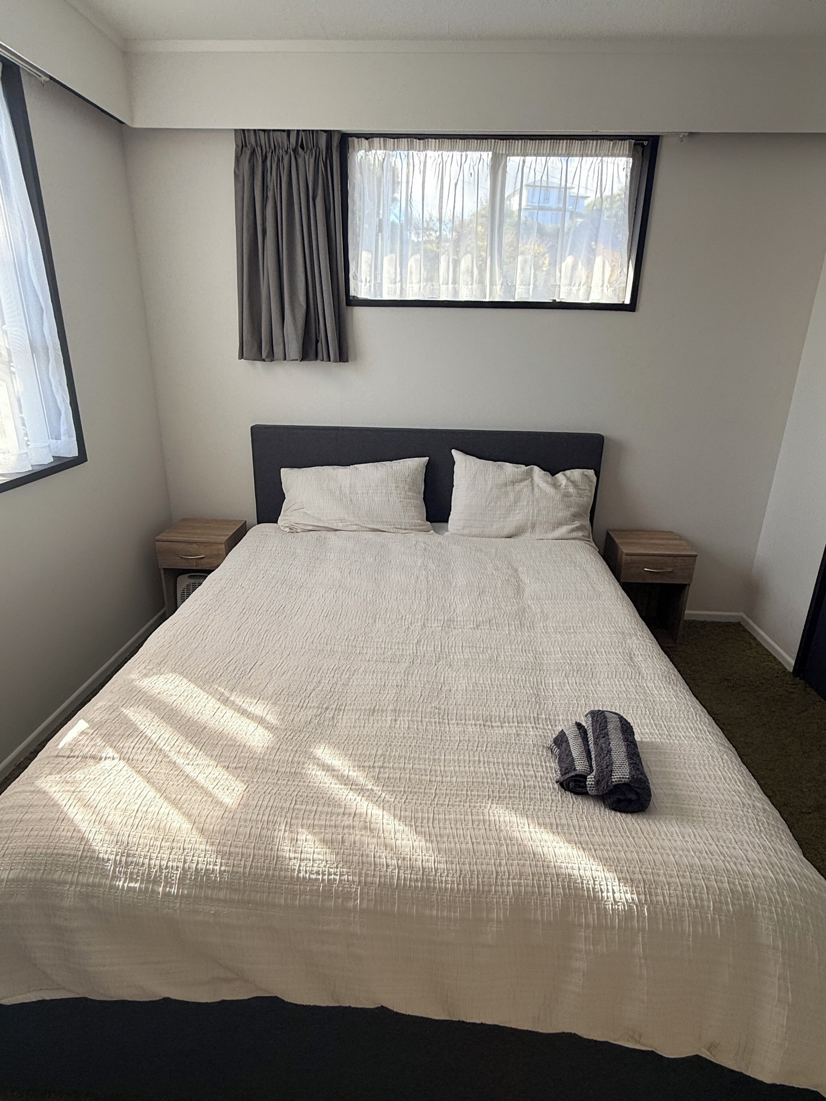 Een slaapkamer met een groot bed, twee nachtkastjes, een raam met gordijnen en uitzicht op de omgeving.