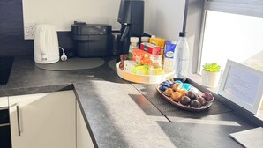 Een moderne keuken met een koffiezetapparaat, een zwarte koffiemachine, een mandje gebak en een kleine potplant.