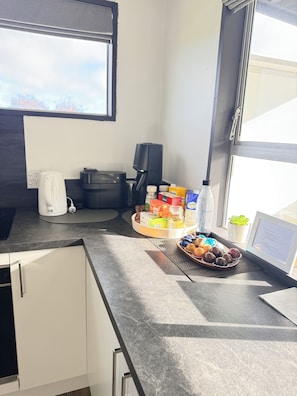 A modern kitchen with a coffee maker, a black coffee machine, a basket of pastries, and a small potted plant.