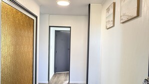Een gang met een houten vloer, een deur, een schoenenrek en twee foto's in lijsten aan de muur.