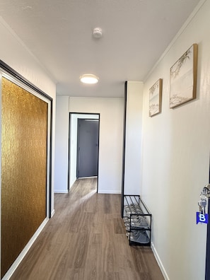 Ein Flur mit Holzboden, einer Tür, einem Schuhregal und zwei gerahmten Bildern an der Wand.