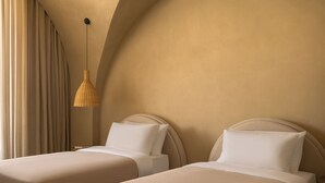 Quarto de hotel com duas camas, luminária pendente e vista para o exterior.