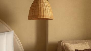 A bedroom with a bed, a bedside table with a book, a brown woven pendant light, and a brown armchair.
