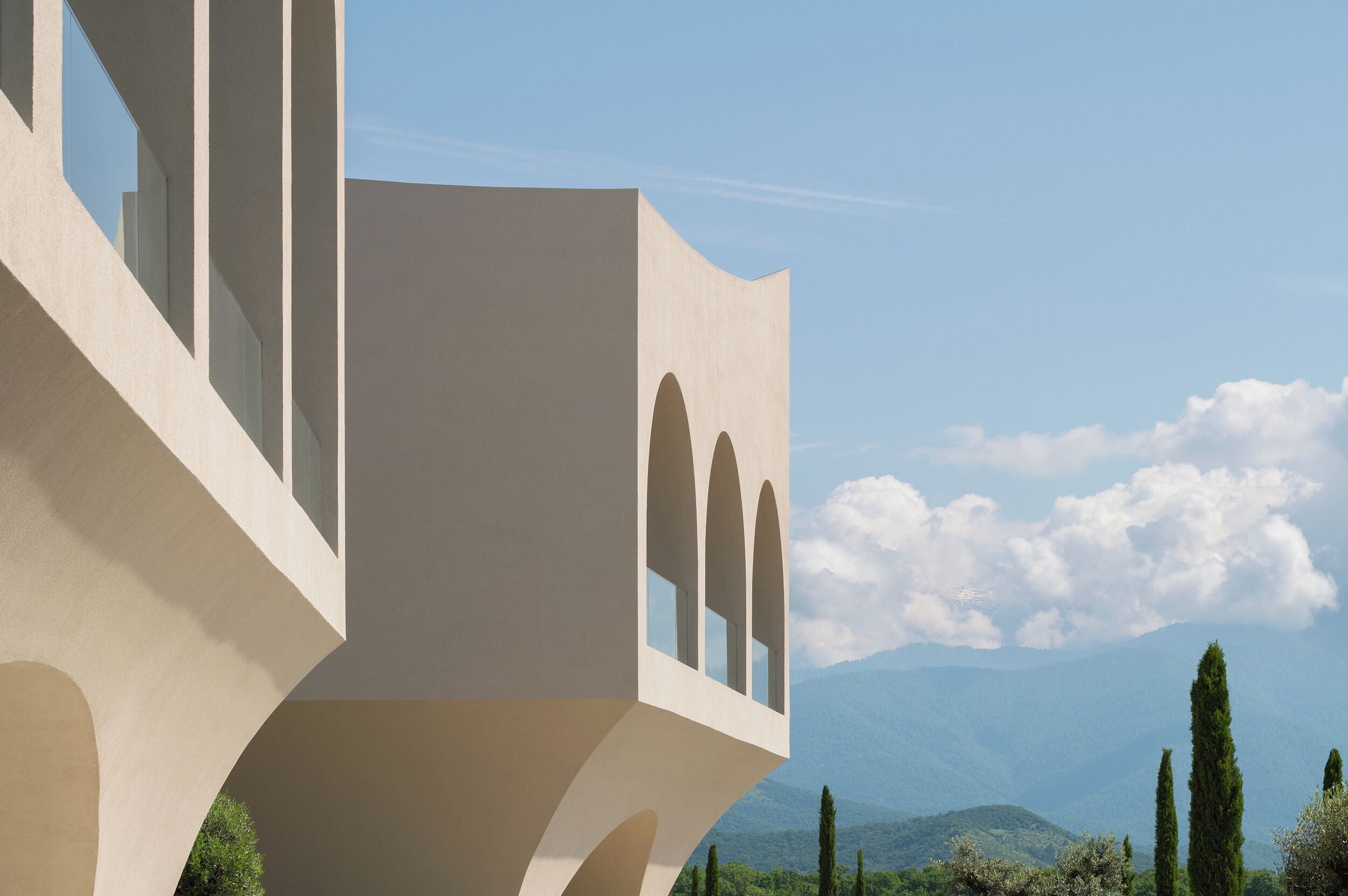 A modern building with a unique architectural design, featuring a balcony with arched windows and a view of distant mountains.