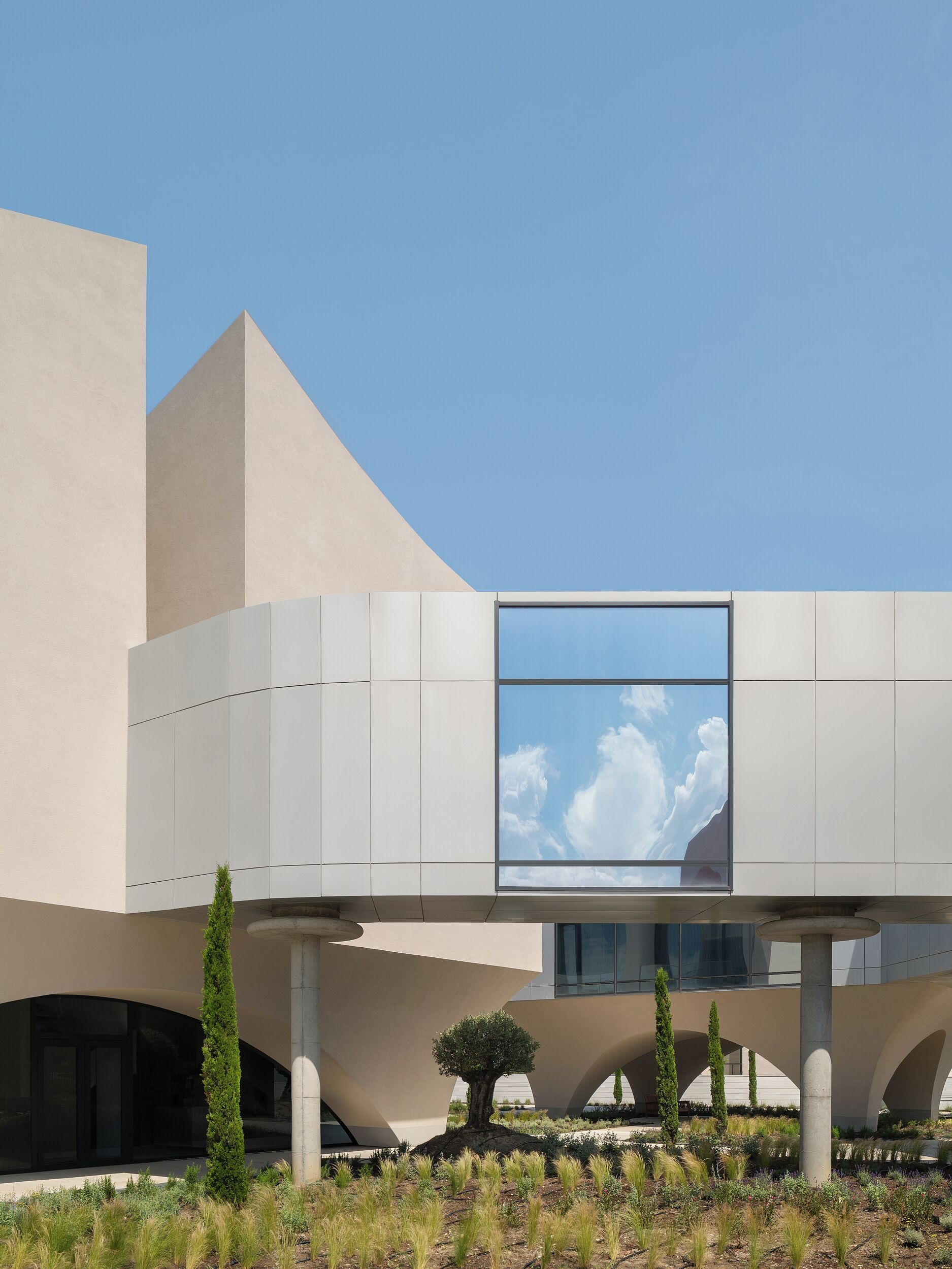 Un edificio moderno con un diseño arquitectónico único, que cuenta con un amplio ventanal y un área ajardinada con plantas.
