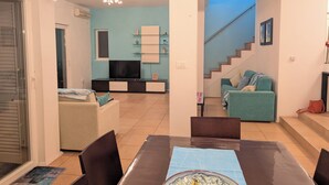 Una sala de estar con televisión, sofá y comedor con sillas y mesa.