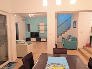 Ein Wohnzimmer mit Fernseher, Sofa und Essbereich mit Stühlen und Tisch.