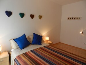 Un lit avec des oreillers bleus, une couvre-lit à rayures, une lampe de chevet et des décorations en forme de cœur accrochées au mur.
