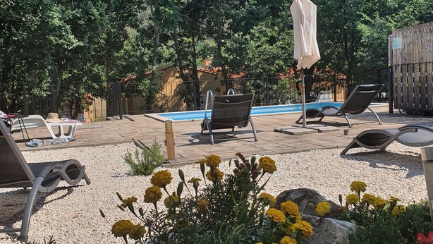 Un área junto a la piscina con sillones de descanso, una sombrilla y un pequeño jardín con flores.
