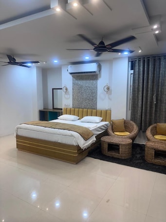 A modern bedroom with a large bed, two wall-mounted fans, an air conditioning unit, and a seating area with wicker chairs.. Hotel Krishna & Restaurant