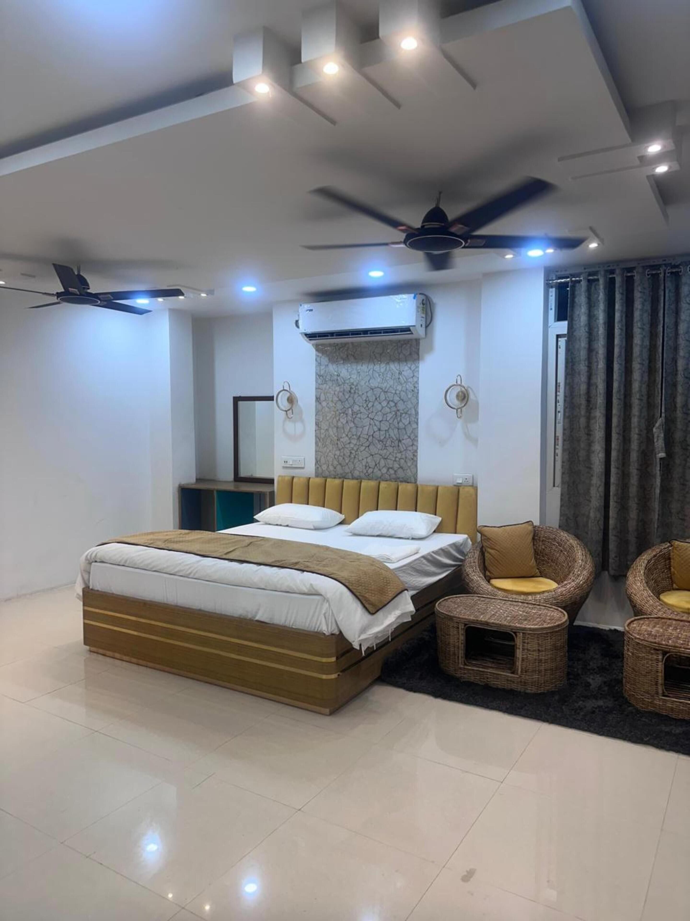 A modern bedroom with a bed, two chairs, a ceiling fan, and an air conditioning unit.