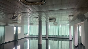 Un amplio salón con piso pulido, ventanas grandes con cortinas y ventiladores de techo.