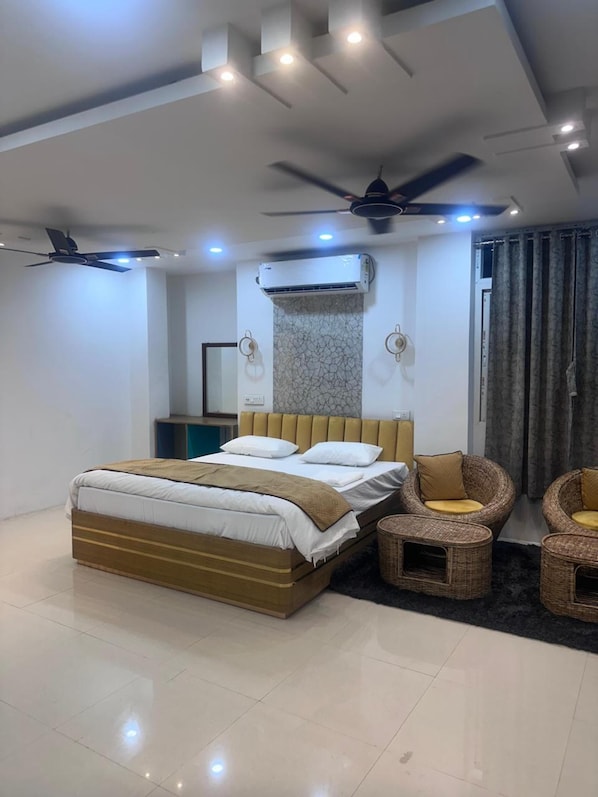 A modern bedroom with a bed, two chairs, a ceiling fan, an air conditioning unit, and a large mirror.