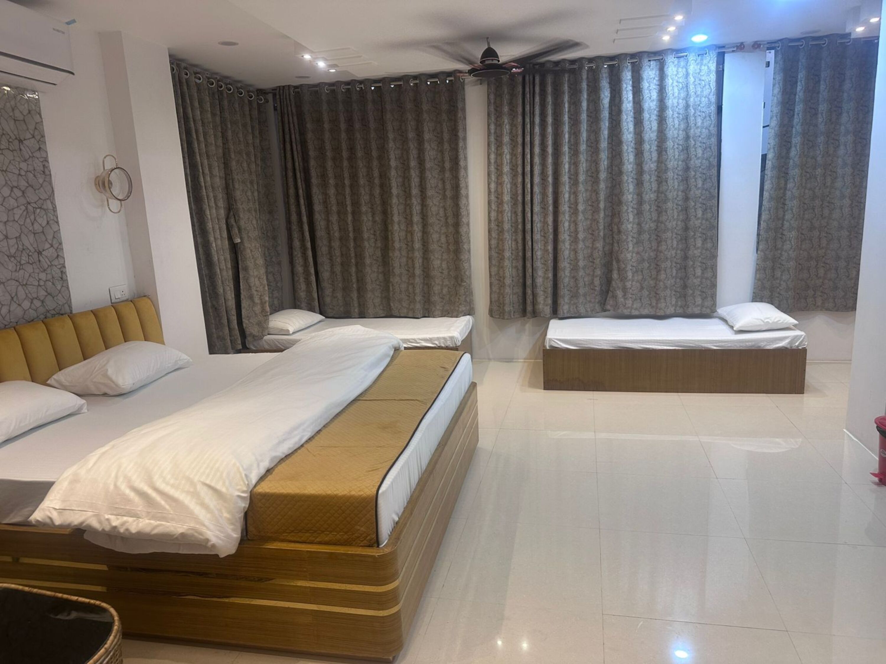 A hotel room with three beds, a ceiling fan, and a large window with curtains.