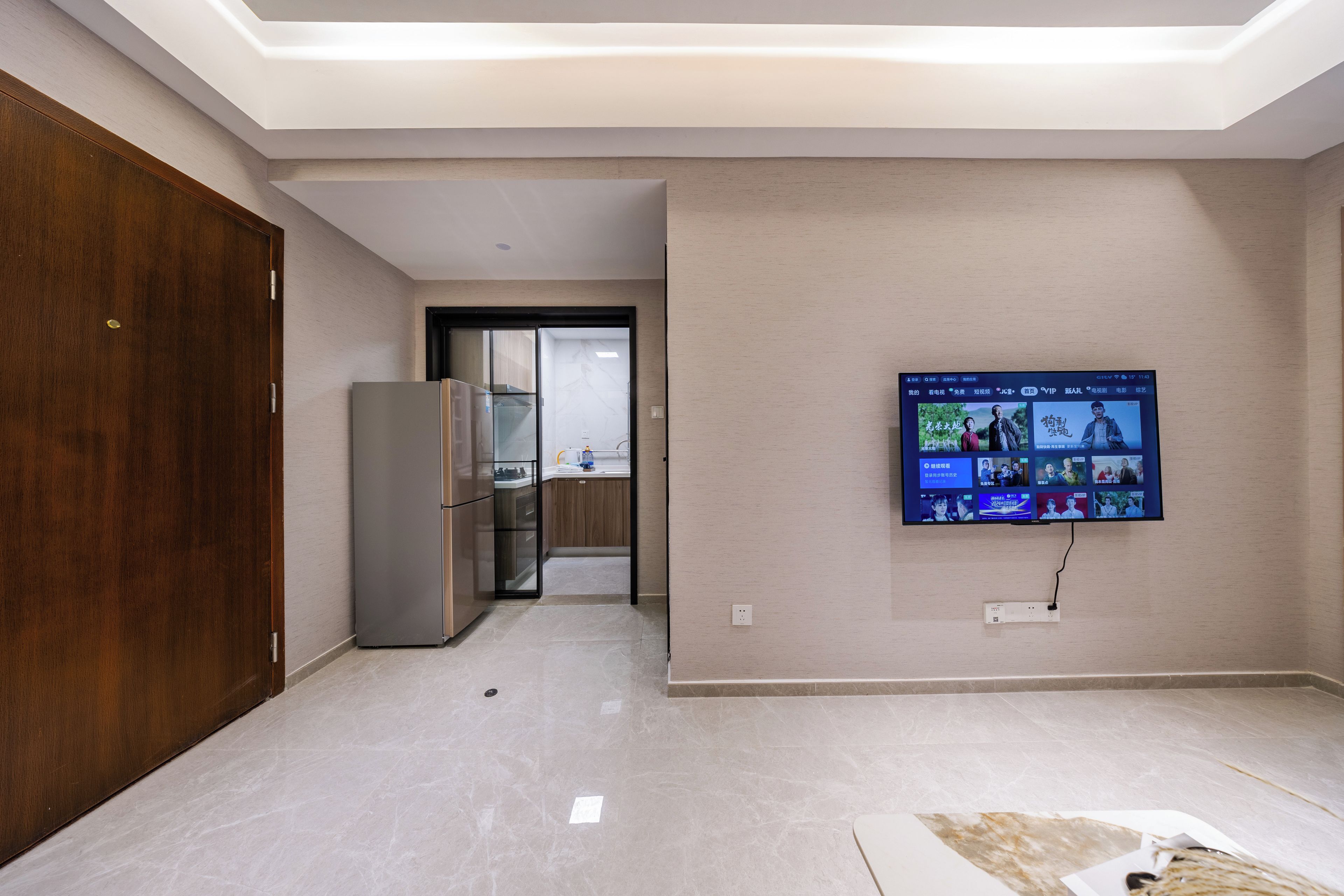 Un soggiorno moderno con una TV a schermo piatto montata a parete, una porta in legno e un frigorifero.