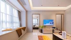 Una habitación de hotel moderna con un ventanal grande, un televisor de pantalla plana, un sofá, una mesita de centro y una mesita de noche.