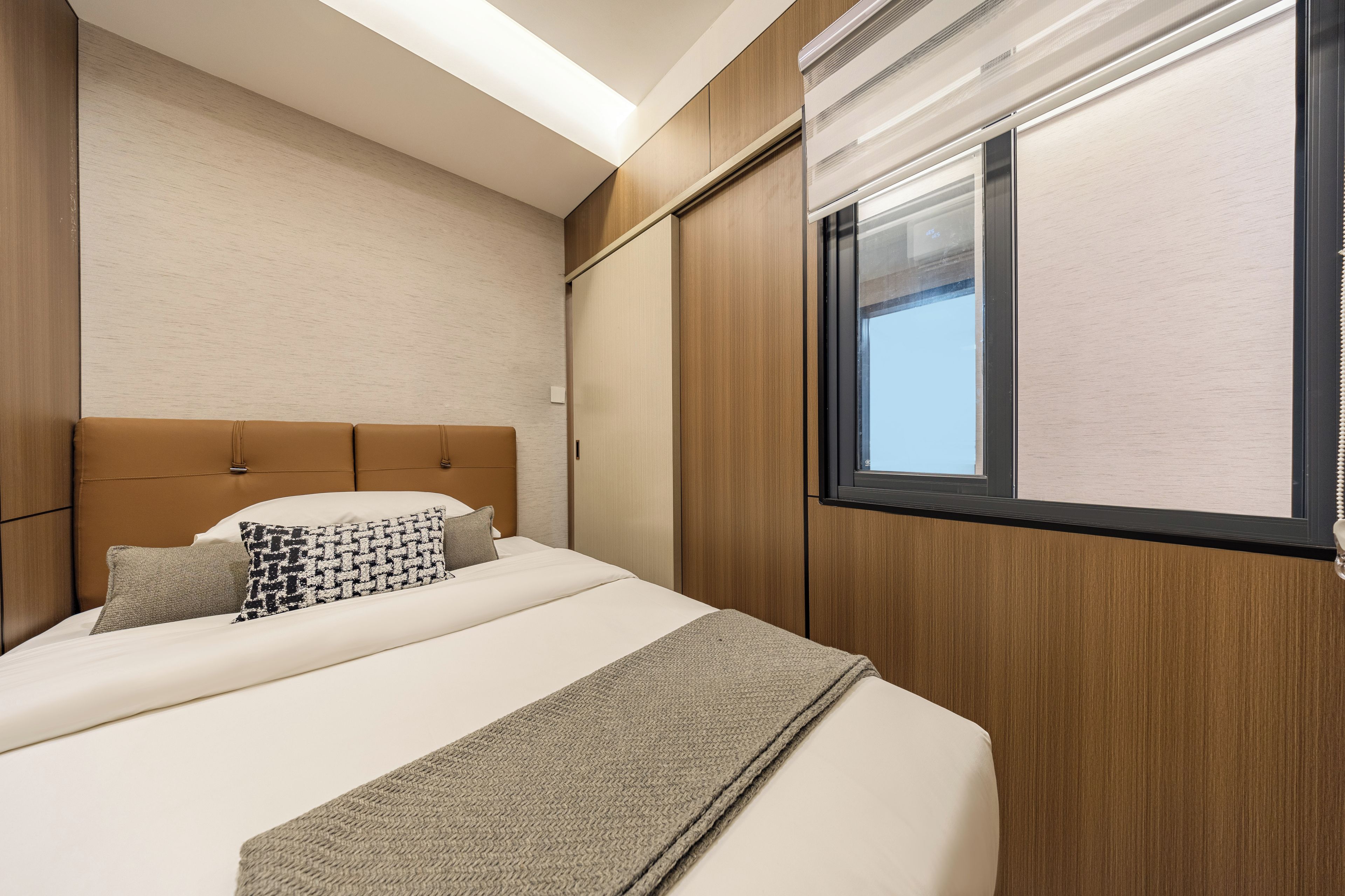 Une chambre d’hôtel comprenant un lit, une tête de lit, une fenêtre et un mur à la finition texturée.