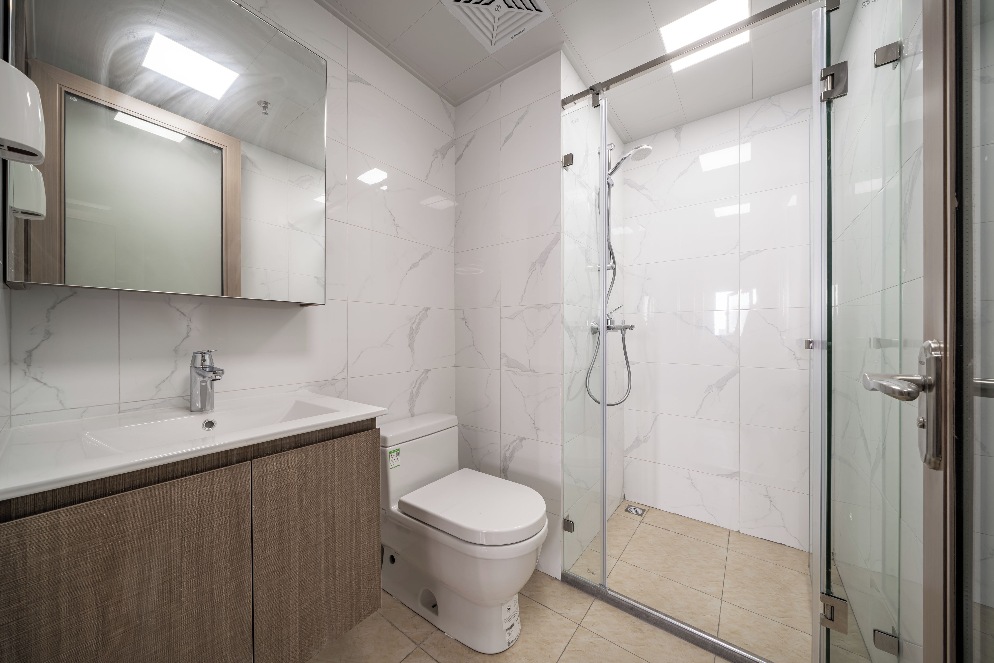 Un baño moderno con ducha envuelta en vidrio, inodoro blanco y tocador con espejo.