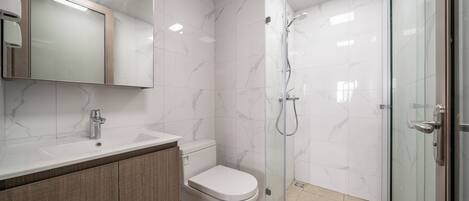 Un baño moderno con ducha envuelta en vidrio, inodoro blanco y tocador con espejo.