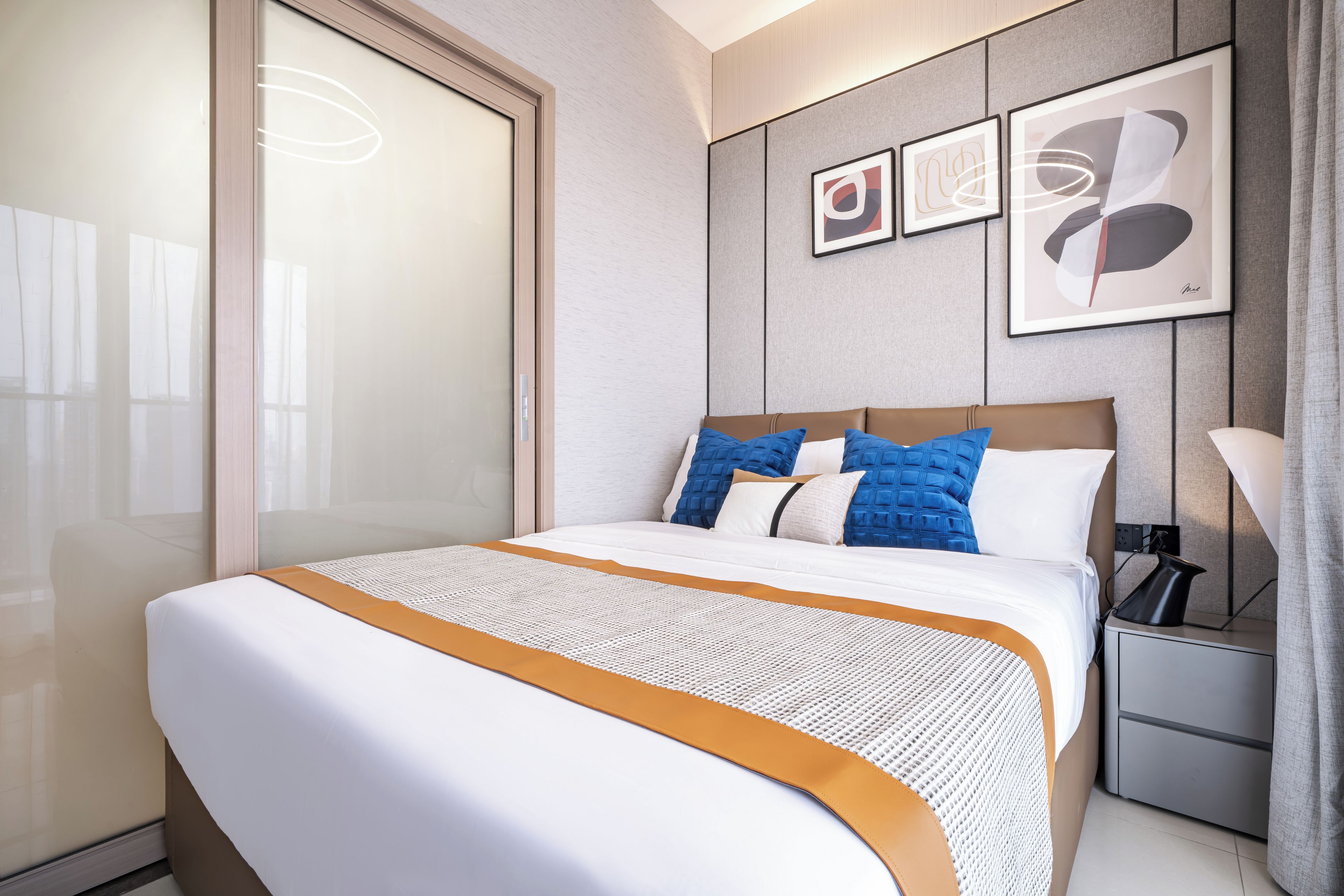 Une chambre d’hôtel avec un grand lit, une table de chevet, une lampe et des œuvres d’art accrochées au mur.