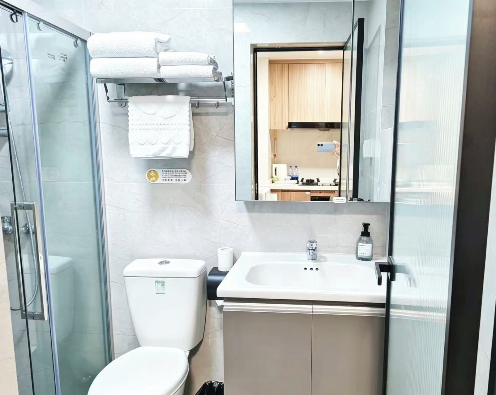 A modern bathroom with a glass shower enclosure, a toilet, a sink with a mirror above, and a towel rack with folded towels.