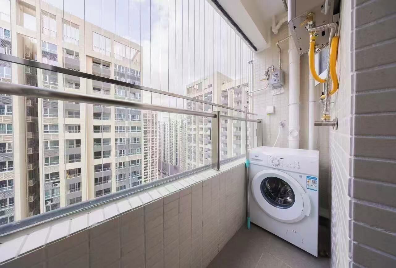 A laundry room with a washing machine, a window with a view of high-rise buildings, and a metal railing.