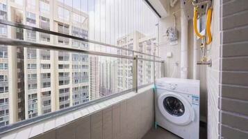 A laundry room with a washing machine, a window with a view of high-rise buildings, and a metal railing.
