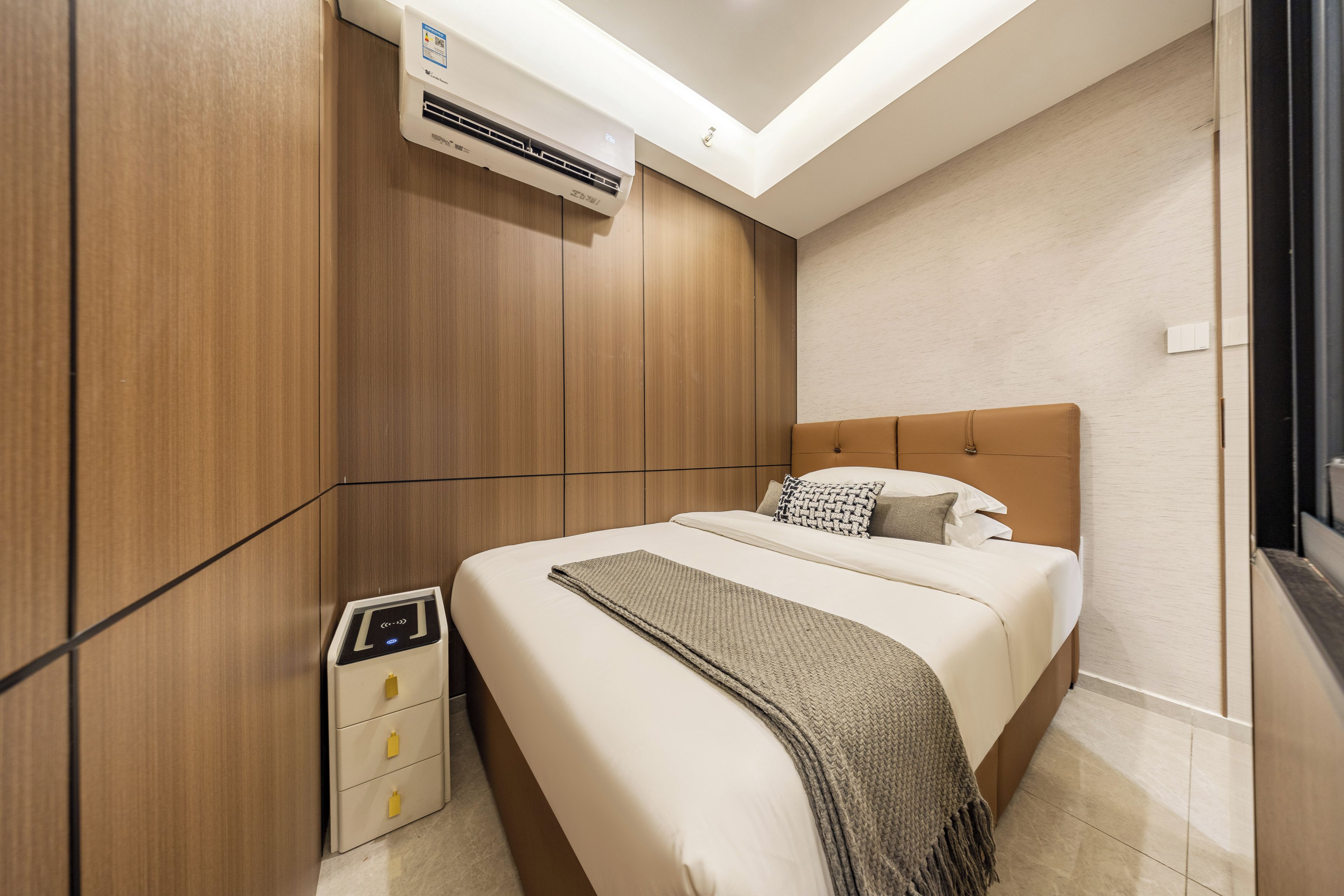 Habitación de hotel con cama, mesita de noche, aire acondicionado de pared y un calentador pequeño.