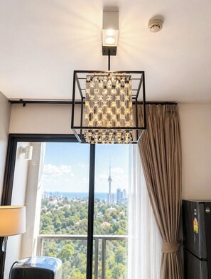 Ein modernes Zimmer mit einem großen Fenster, einer außergewöhnlichen geometrischen Leuchte und Blick auf eine Stadtansicht.
