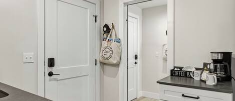 Un couloir avec des portes blanches, un coin café équipé d’une machine à café et un sac accroché au mur.