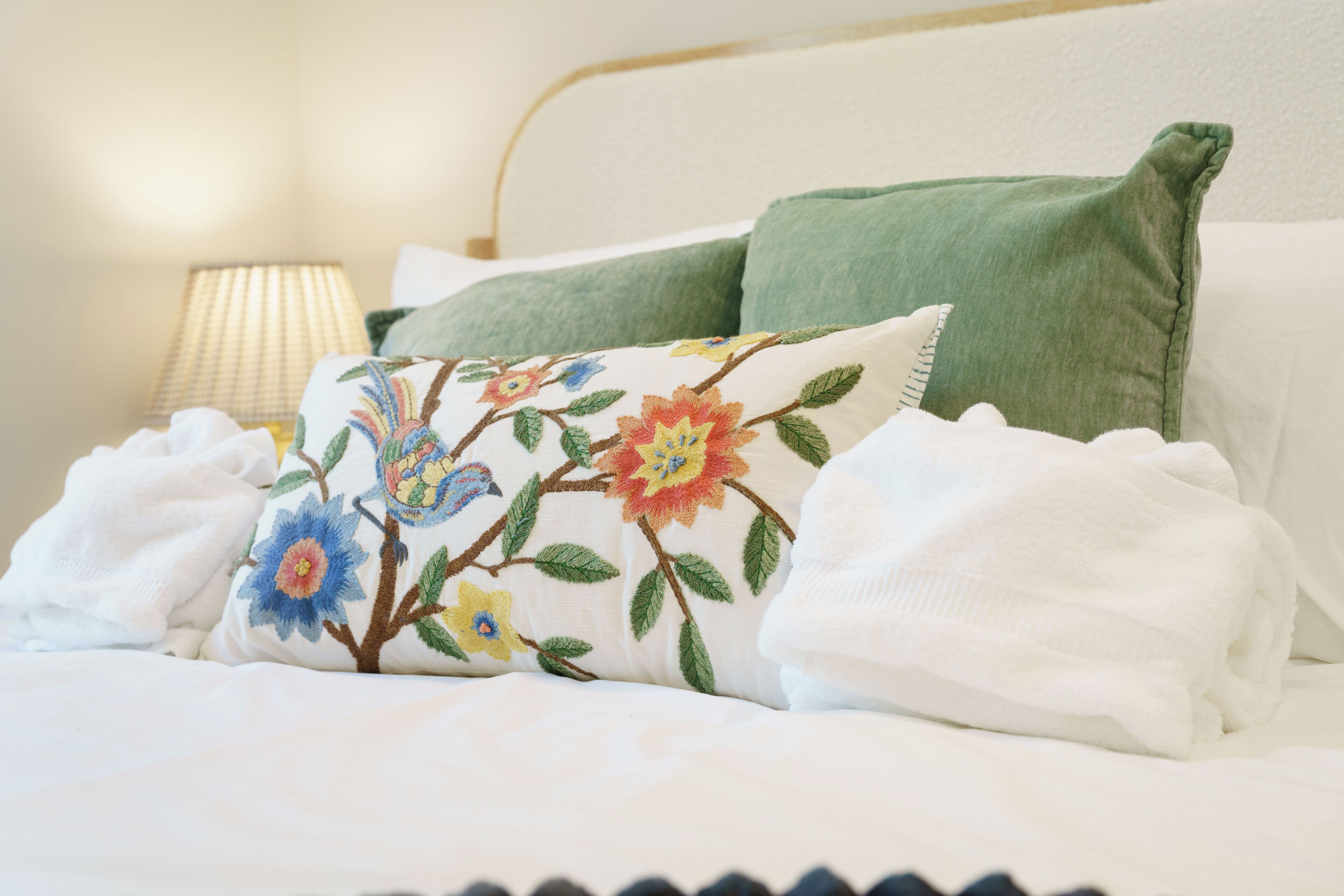 Ein ordentlich gemachtes Bett mit blumigen Kissen, einer grünen Decke und einem weißen Handtuch.