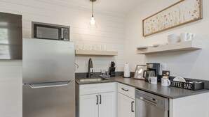 A modern kitchen with a stainless steel refrigerator, microwave, and dishwasher. There are white cabinets, a sink, and a coffee bar with mugs and a coffee maker. - Birch @ Timberline Flats (Traverse City)