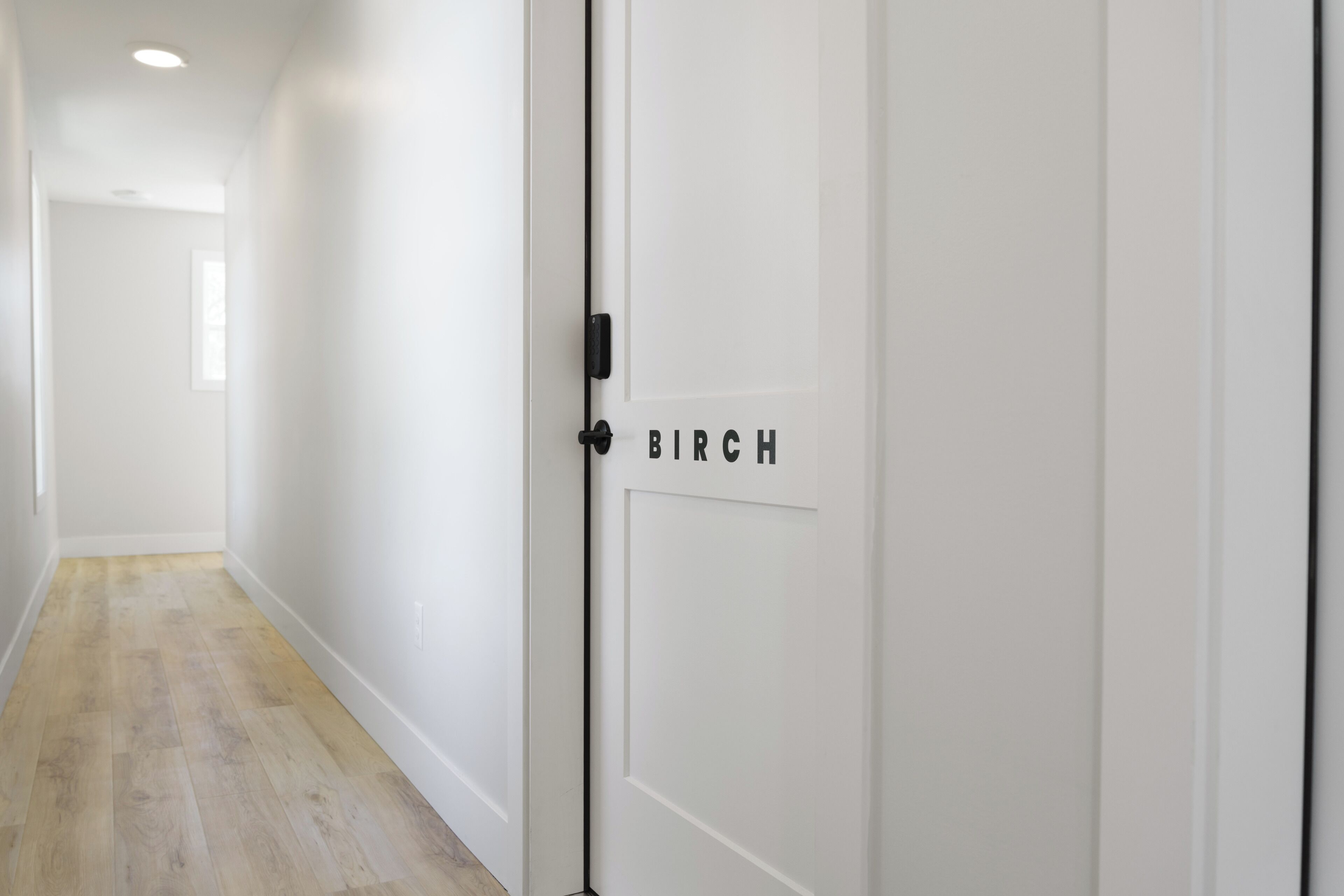 Un couloir avec une porte blanche portant l’inscription « BIRCH » et un plancher en bois.