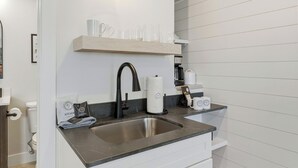 Eine moderne Küche mit Spüle aus Edelstahl, einem schwarzen Wasserhahn, einem Holzboden mit Gläsern und einer Kaffeemaschine.