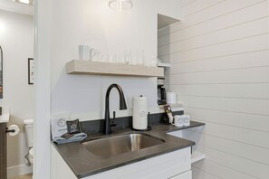 A modern kitchen with a stainless steel sink, a black faucet, a wooden shelf with glassware, and a coffee maker. - Timberline 4 upper Units (Traverse City)