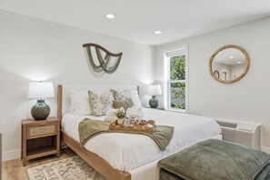 Une chambre à coucher comprenant un lit, des tables de chevet, une fenêtre et un miroir fixé au mur.