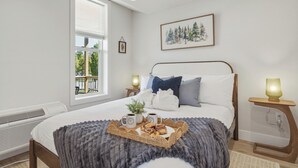 Ein Schlafzimmer mit einem Bett, einem Fenster, einem gerahmten Bild, Nachttischen und einem Tablett mit Speisen und Getränken.