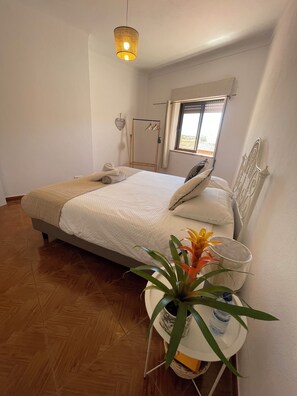 Ein Schlafzimmer mit einem Bett, einem Nachttisch mit Pflanze, einer Pendelleuchte und einem Fenster mit Aussicht.