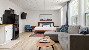 A modern hotel room with a kitchenette, a bed with a headboard, a grey sofa, a small wooden table, and a painting on the wall. - Timberline 3 Lower Units (Traverse City)