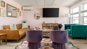 A living room with a sofa, ottoman, coffee table, and a TV mounted on the wall. - Timberline 3 Lower Units (Traverse City)