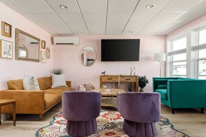 Ein Wohnzimmer mit Sofa, Hocker, Couchtisch und einem an der Wand montierten Fernseher.