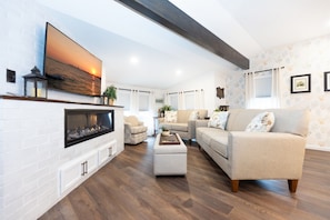 Ein Wohnzimmer mit Kamin, einer Couch, einem Couchtisch und einem an der Wand befestigten Fernseher.