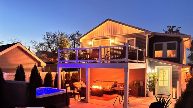 A two-story house with a covered patio, outdoor seating, and a hot tub. - Sirens Keep | Boutique Style Outdoor Living • Hot Tub • Sleeps 8 (Delhaven)