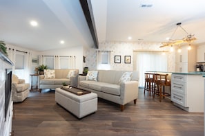 Ein modernes Wohnzimmer mit einer Couch, einem Hocker und einem Essbereich mit Stühlen und einem Tisch.