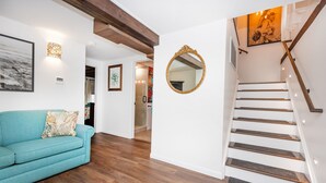 A staircase with wooden steps and a handrail, a blue sofa with a patterned cushion, and a wall-mounted mirror. - Sirens Keep | Boutique Style Outdoor Living • Hot Tub • Sleeps 8 (Delhaven)