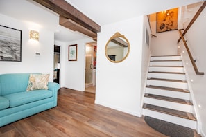 Eine Treppe mit Holzboden und Handlauf, ein blaues Sofa mit einem gemusterten Kissen und ein an der Wand befestigter Spiegel.