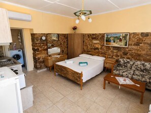 Une chambre à coucher avec un lit, une commode en bois, une table de chevet, un canapé, une petite table, un lave-linge et un mur en pierre.